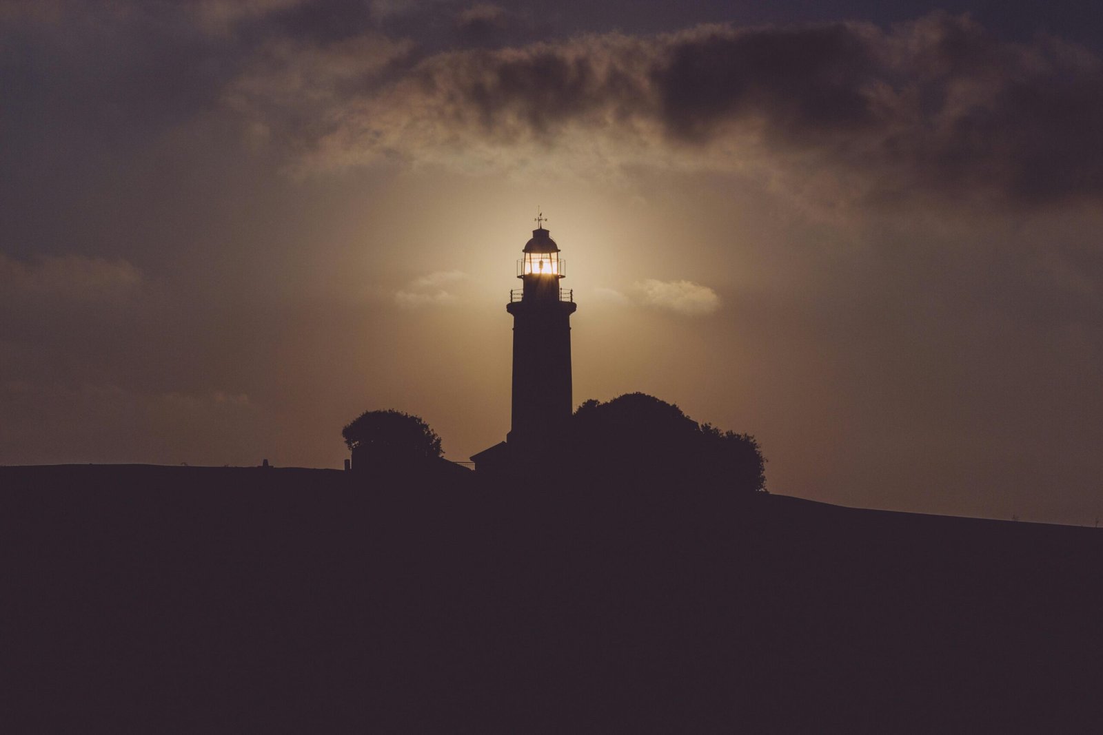 A dramatic silhouette of a lighthouse against a sunset sky, creating a moody and atmospheric scene.