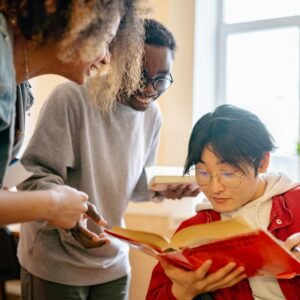 Three students engaging with books in a bright university library setting.
