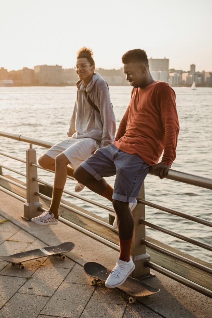 Two young skateboarders enjoying leisure time by the waterfront railing during sunset.