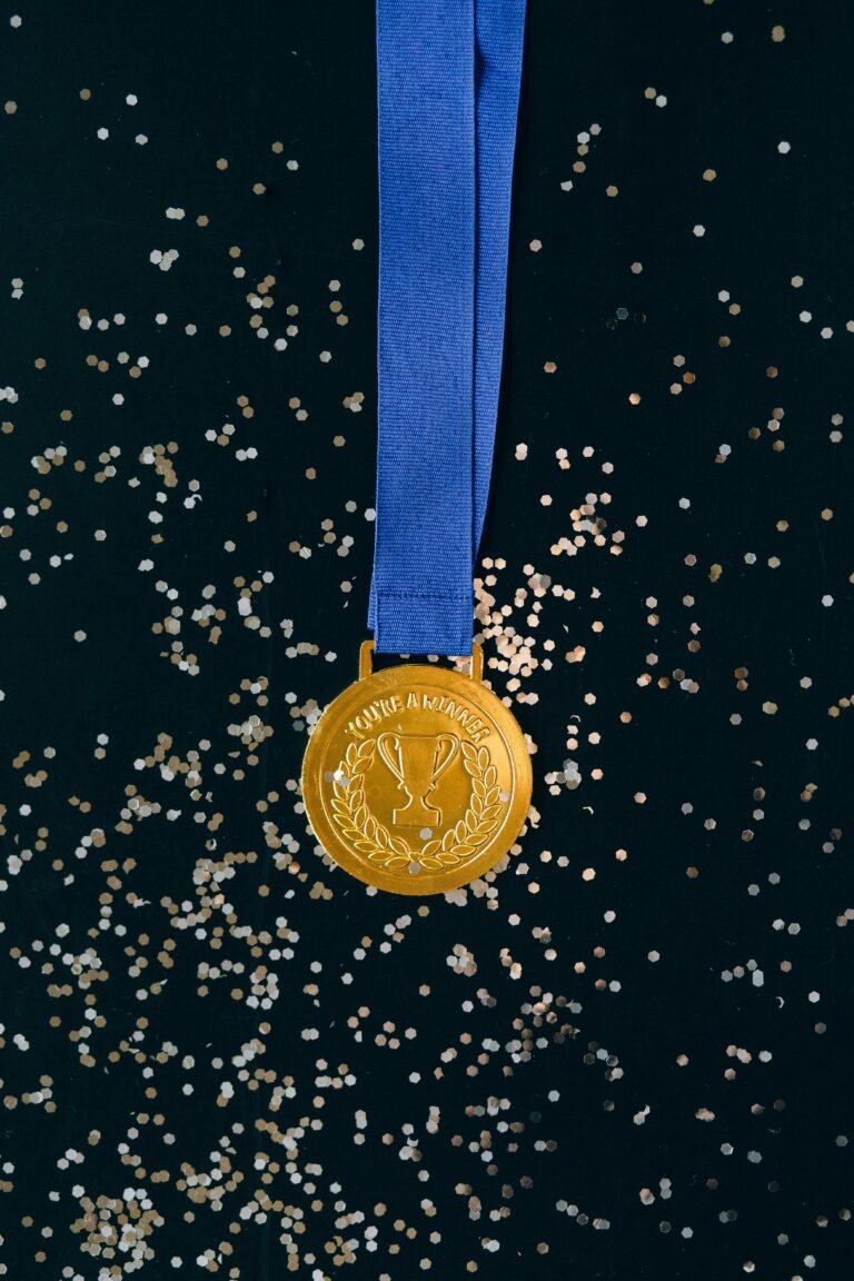 Close-up of a shimmering gold medal with blue ribbon on a black surface, symbolizing victory and achievement.