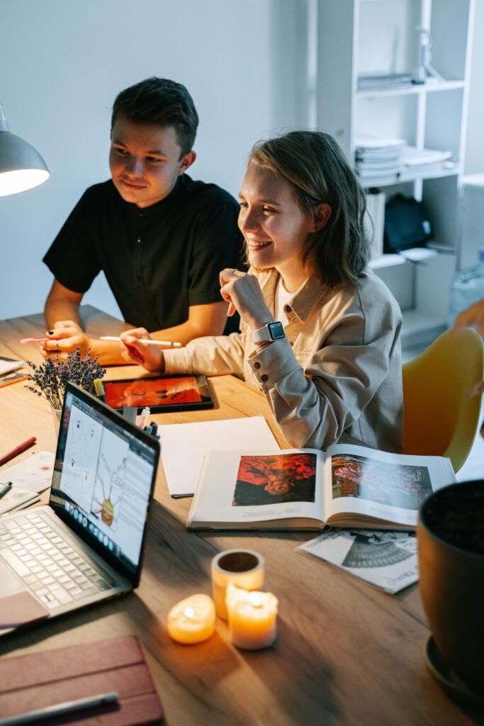 Two young professionals working together in a cozy, modern workspace with laptops and books.