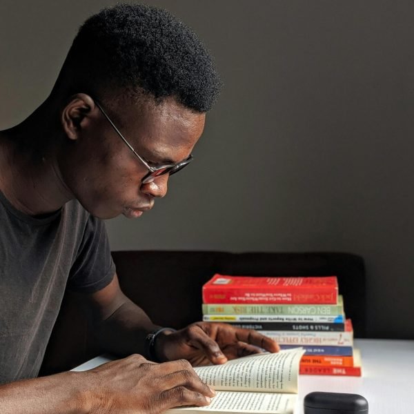 Young man studying intently with books in library setting.
