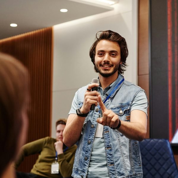A confident speaker engaging with the audience during an indoor conference, using a microphone.